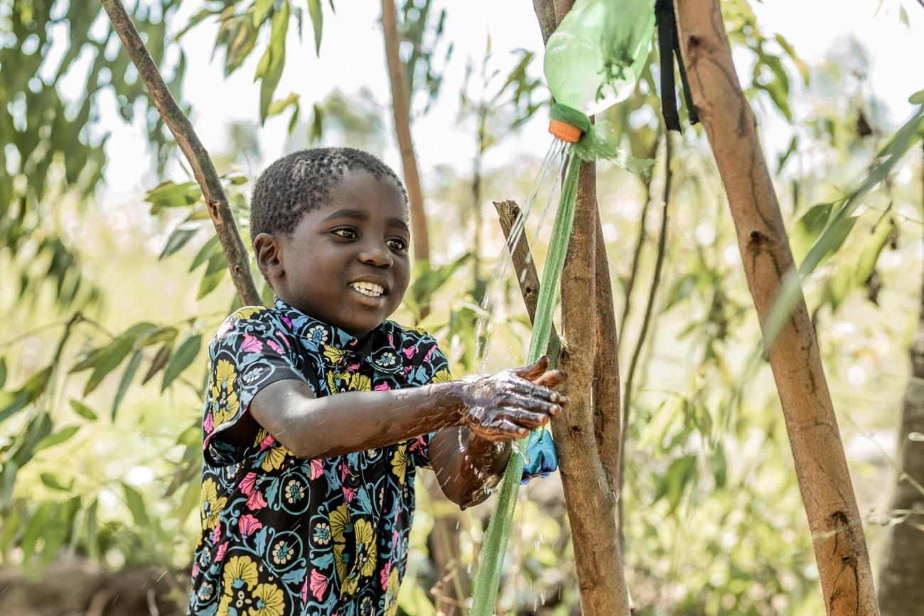 Olive's son, five-year-old Phineas Mpomba washing his hand by the tippy-tap constructed by chikondi caregroup members under Afikepo. This initiative ensures access to clean water for proper hygiene after toilet use.