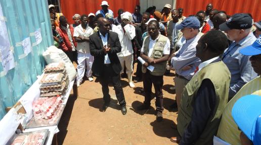 Ambassador Scott in dark blue cap listens to UNHCR Livelihood Officer Richmond Msowoya on livelihood activities being implemented in Dzaleka.